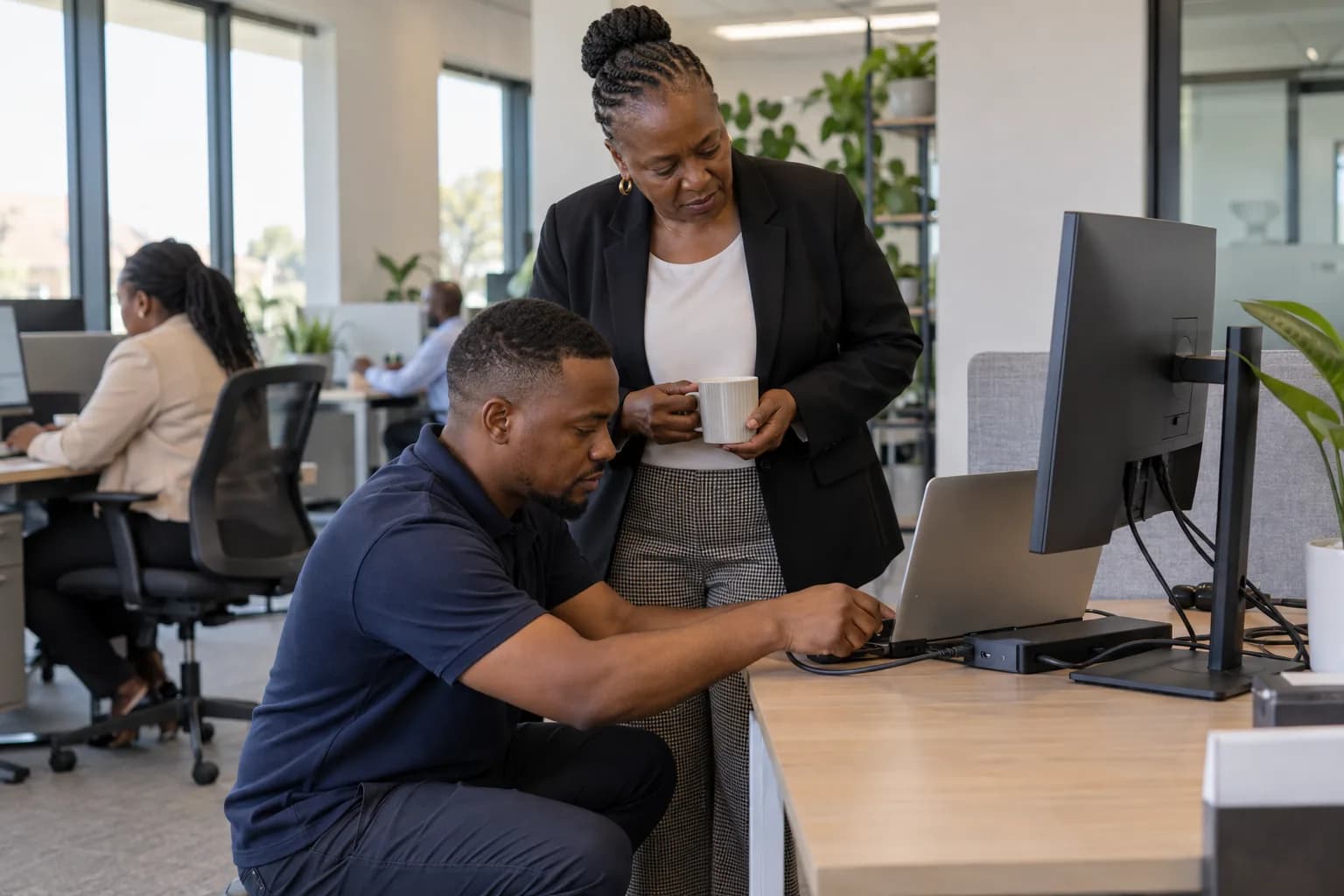 An IT technician setting up a laptop for a staff member at their desk.